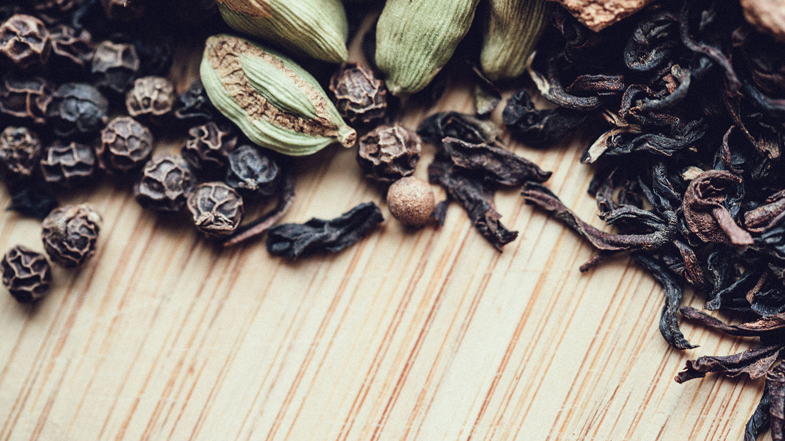 Cloves cardamom and peppercorns on a timber board