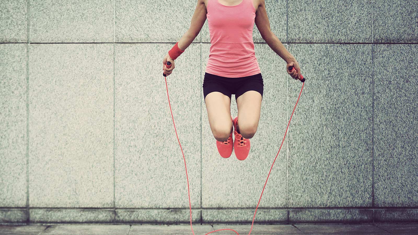 Girl skipping rope in front of wall